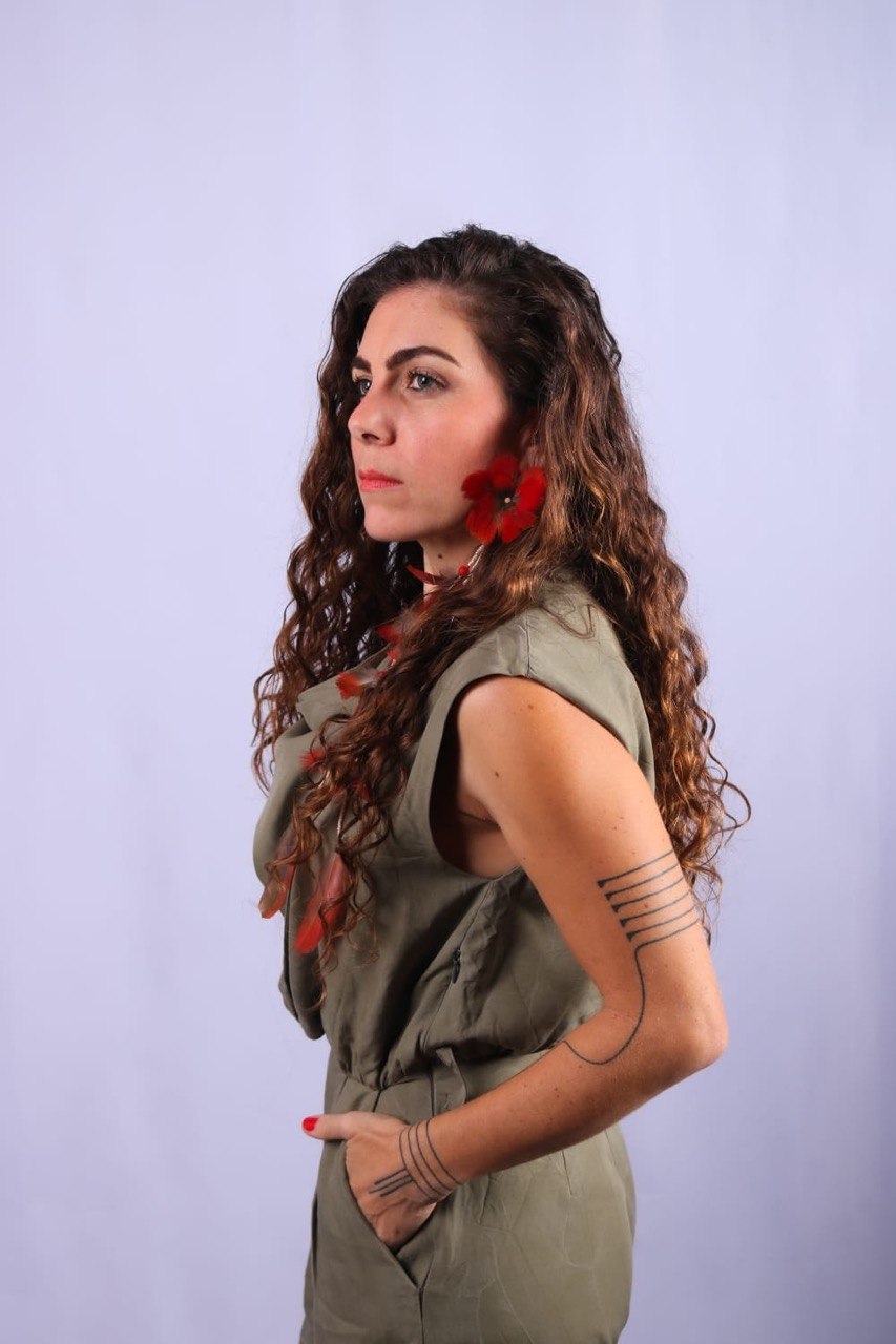 Flávia Maitri em retrato de perfil, expressão serena, brincos de pena vermelha